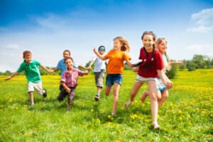 A group of kids in summer clothes running and playing on the green grass under a blue sky